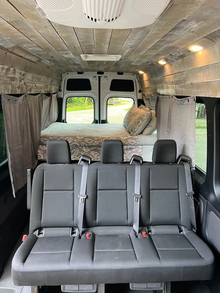 Spacious rv rental interior: custom wood-paneled camper van with rear bed & 3-person seating.
