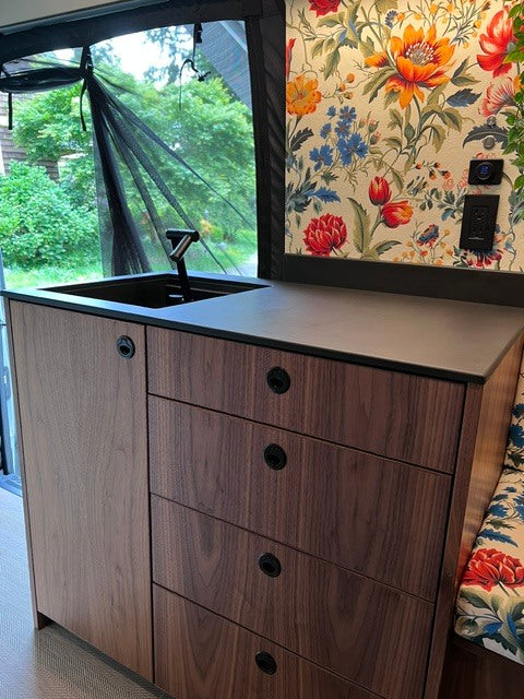 Cozy rv rental kitchen: dark wood cabinets, sink, and vibrant floral wallpaper, with a view to nature.