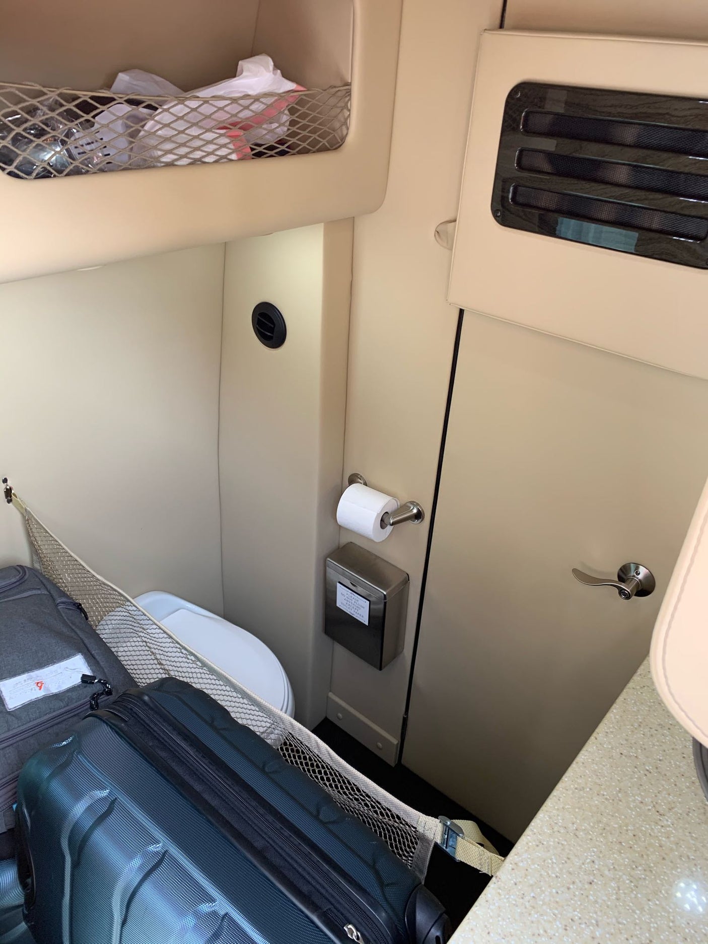 Compact RV rental interior shows a small toilet, storage nets with luggage, and built-in cabinets, optimizing space for travel.