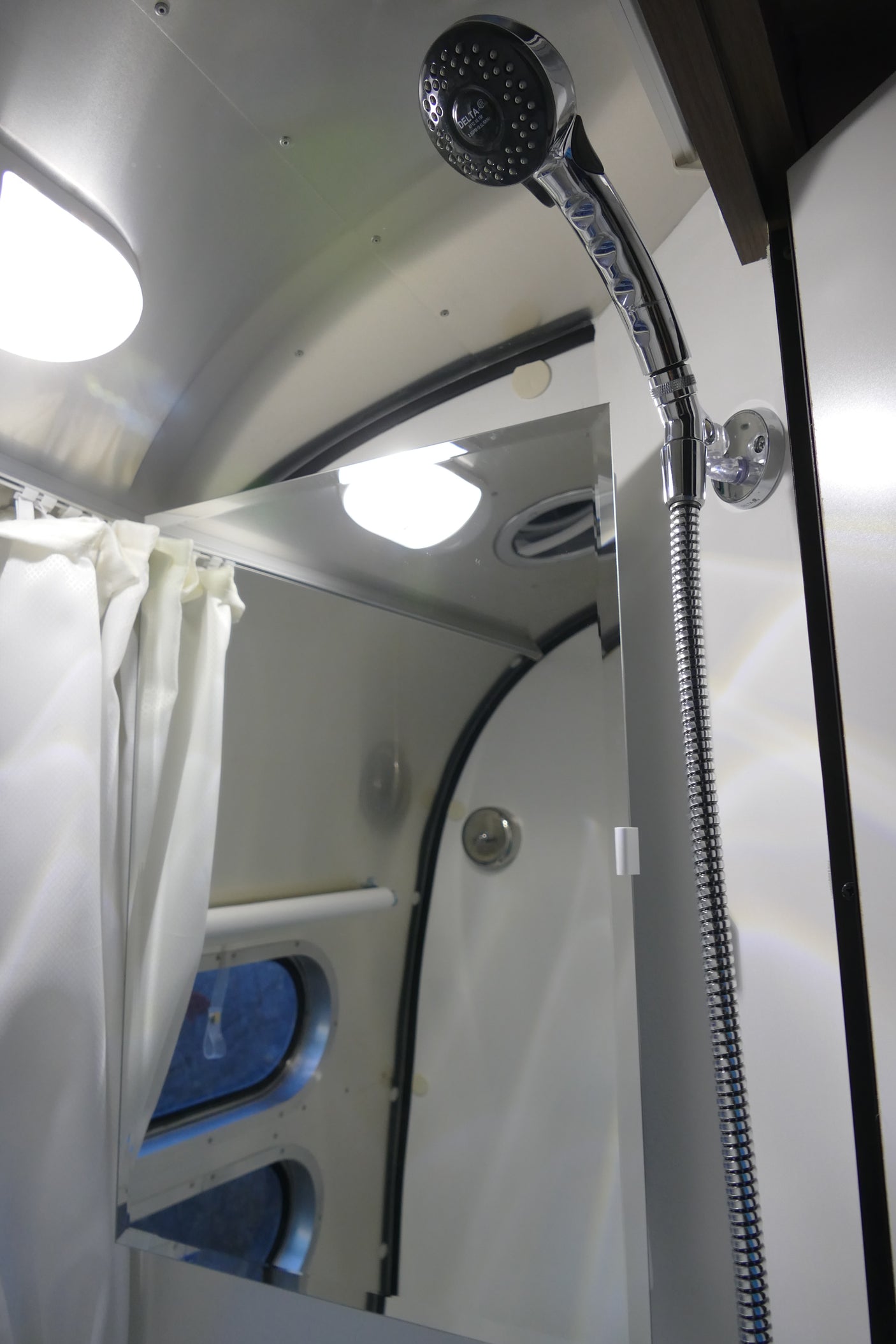 RV rental shower features a modern chrome showerhead, white curtains, and mirror reflecting bright interior lights.