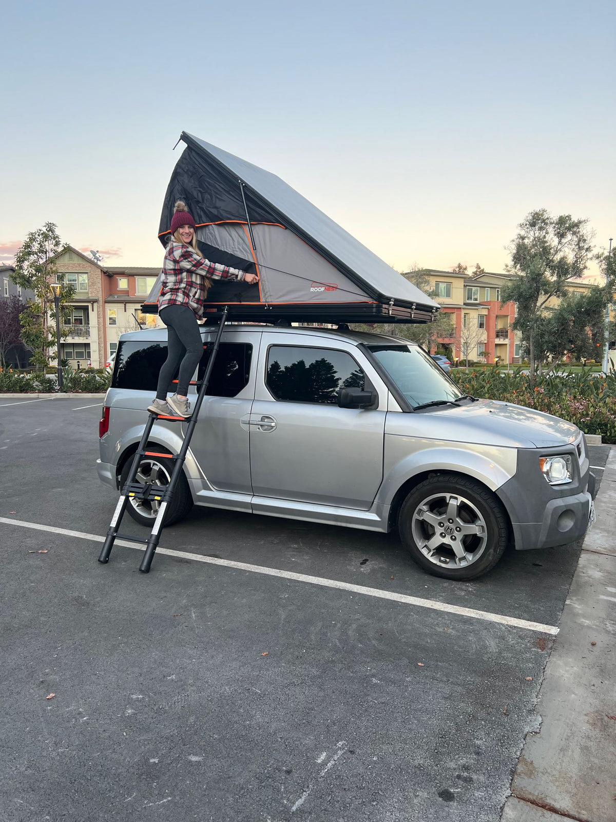 A woman sets up a Roofnest rooftop tent on a silver Honda Element