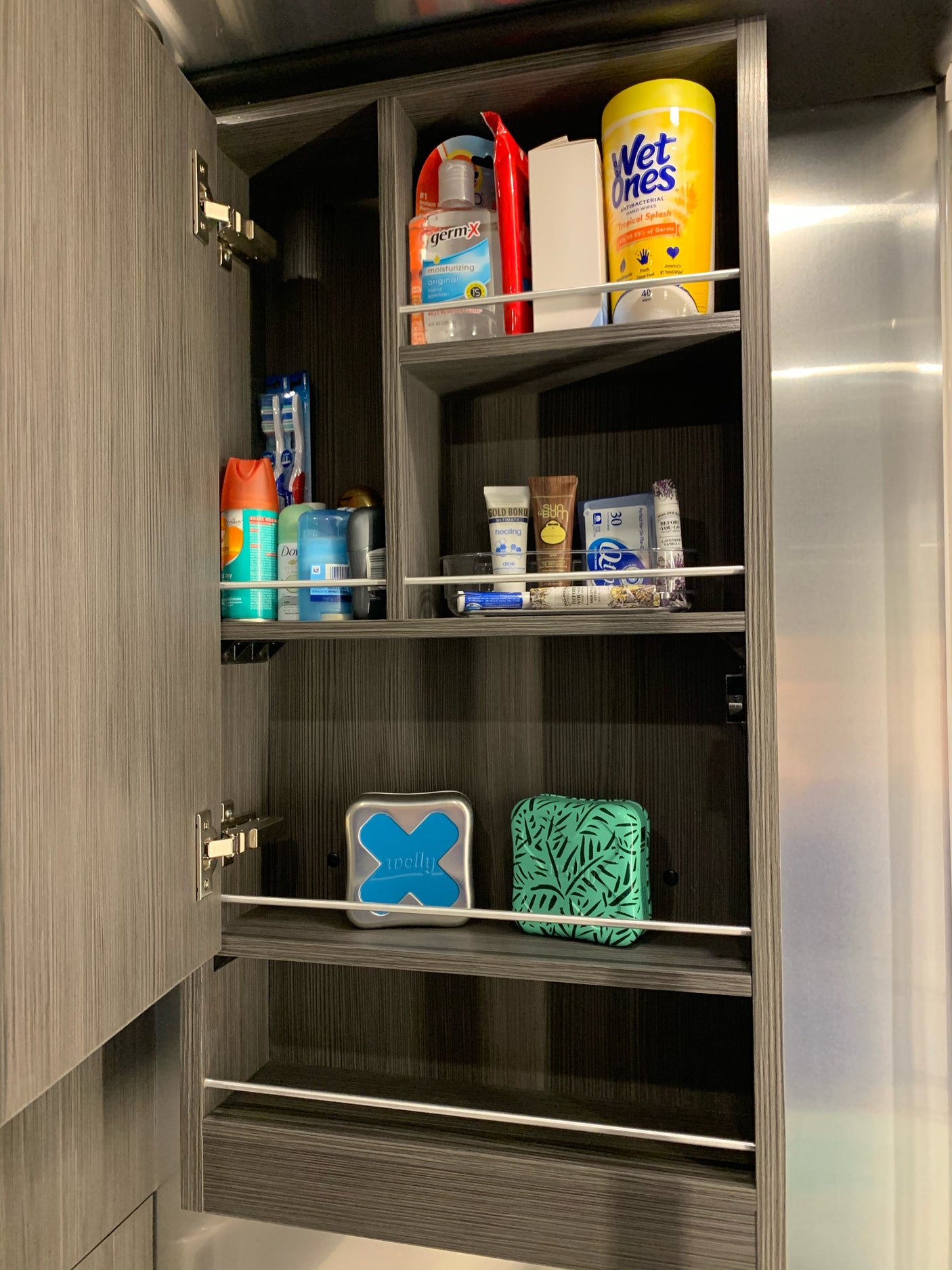 RV rental bathroom cabinet, efficiently organized with hand sanitizer, wipes, deodorant, and oral hygiene products on shelves.