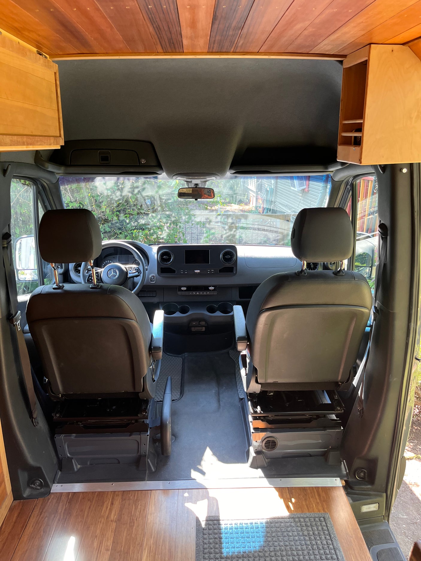 Front cabin of an RV rental, showcasing driver/passenger seats, dashboard, & custom wooden interior.