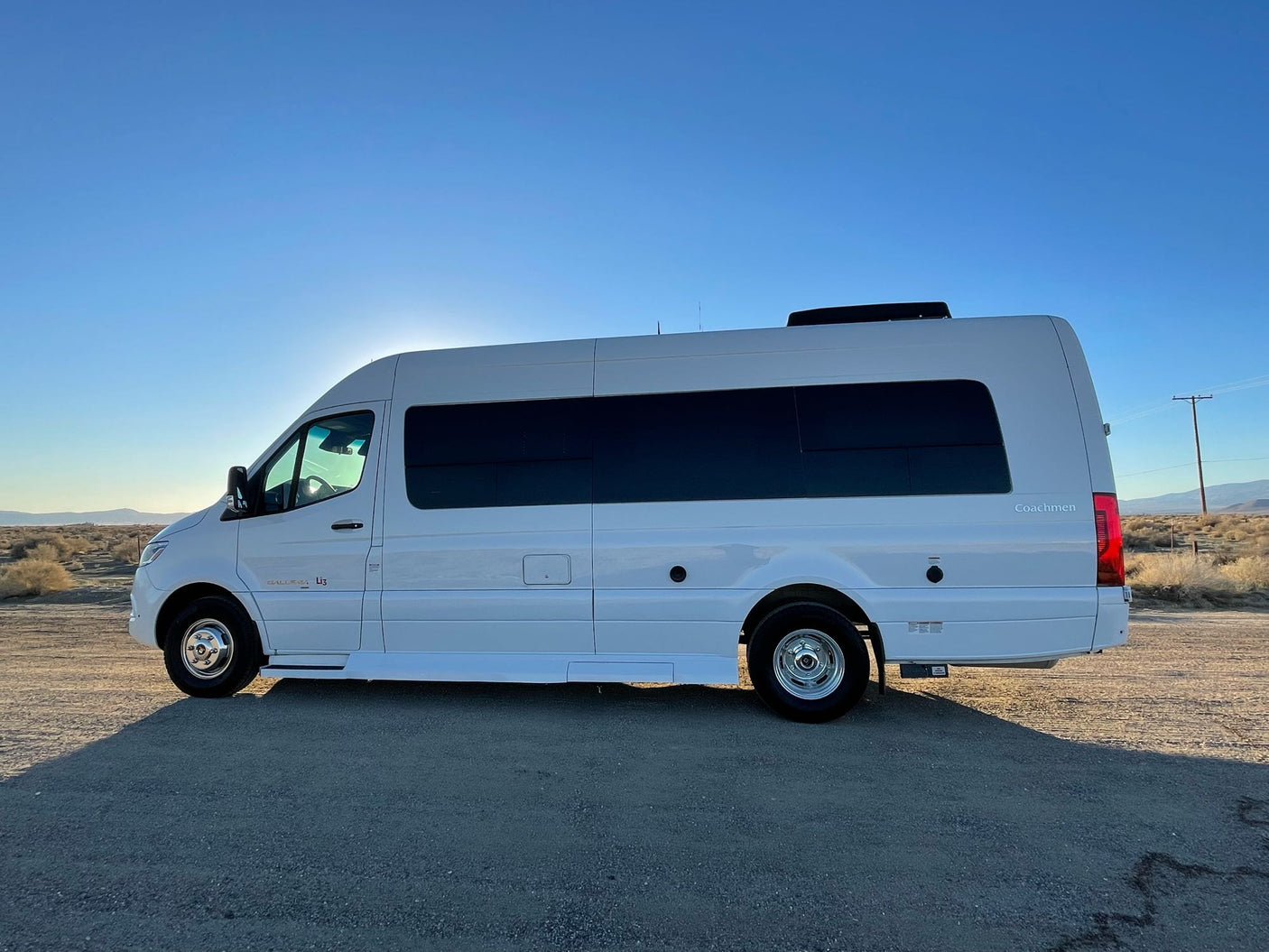 White Coachmen Galleria RV rental parked on a dirt road in a sunny desert landscape under a clear blue sky. Perfect for adventure!