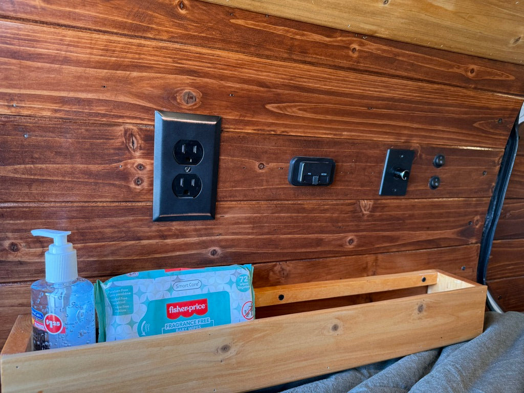 Inside this RV rental, find a rich wood wall with essential power outlets, charging ports, and a handy bedside shelf.