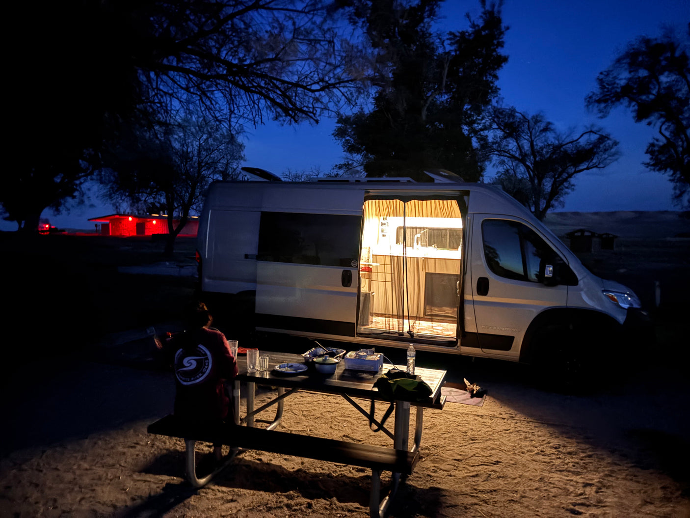 Van life evening: cozy rv rental lights up a picnic dinner under a twilight sky. Perfect for camping adventures.