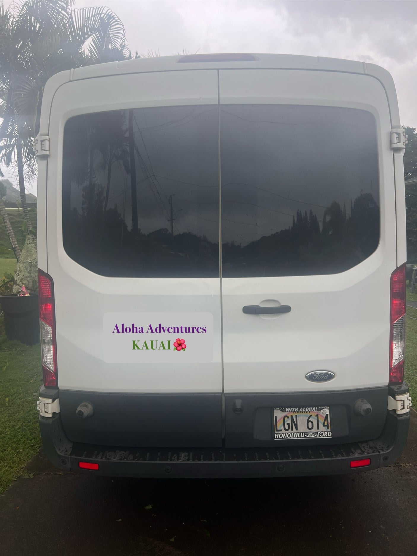 This white Ford van RV rental, with an "Aloha Adventures Kauai" sticker, features Hawaii license plate LGN 614.