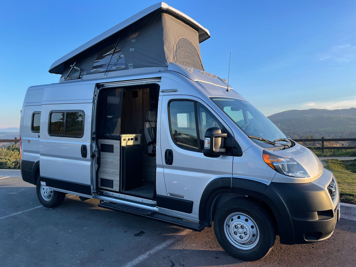 Silver pop-top camper van, perfect for an rv rental adventure, with its side door open revealing a cozy interior.
