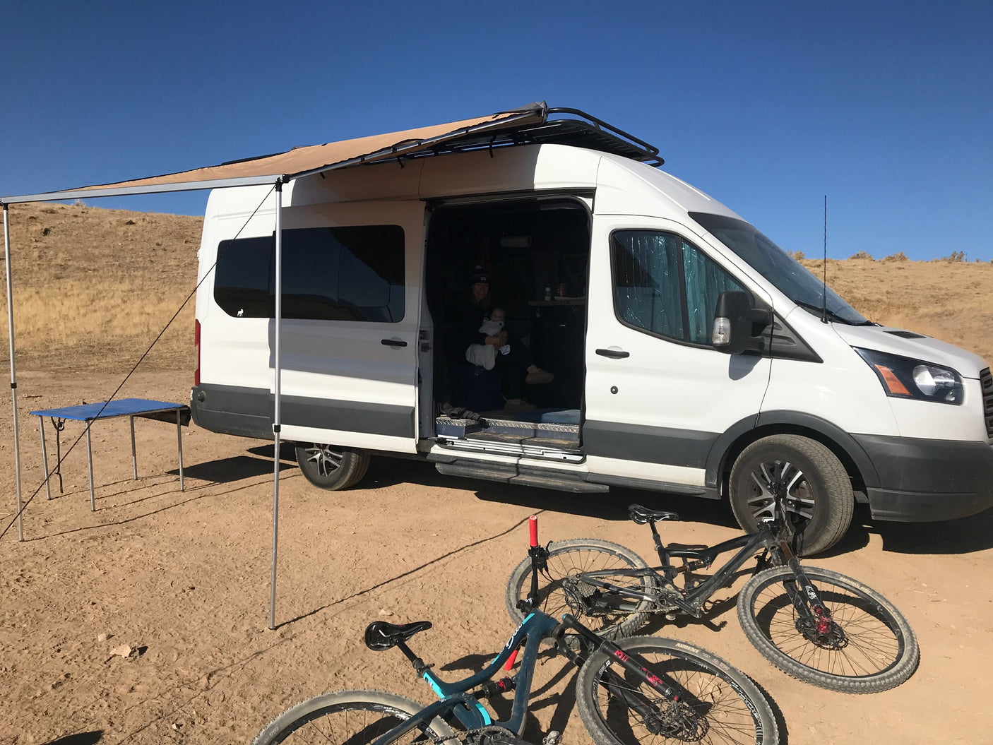 **RV rental** fun: A converted van with an awning, family, and bikes for outdoor adventures in the desert. Perfect for van life camping.