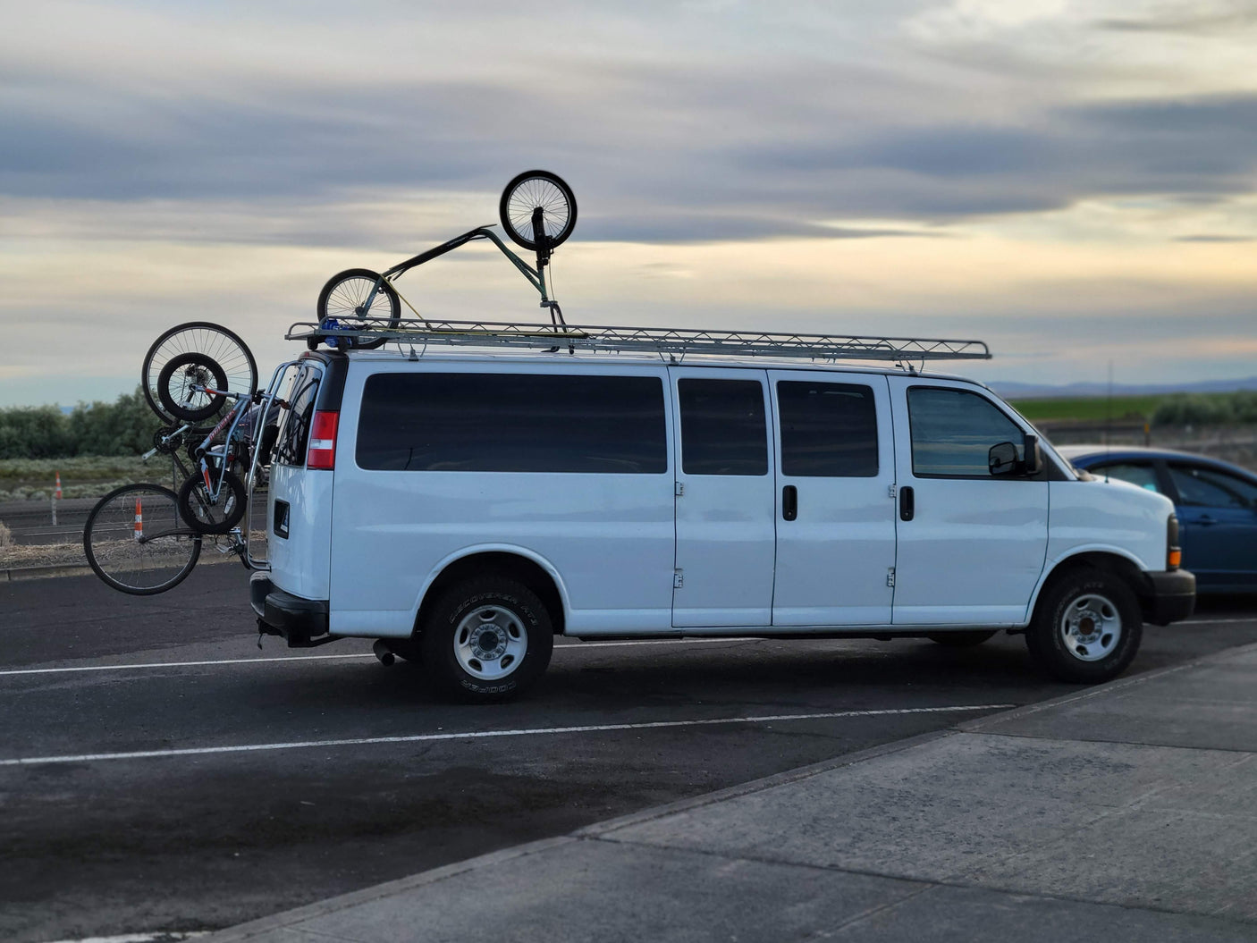 White conversion van with roof rack & rear bike rack, carrying multiple bicycles, suggesting an RV rental for outdoor adventures.