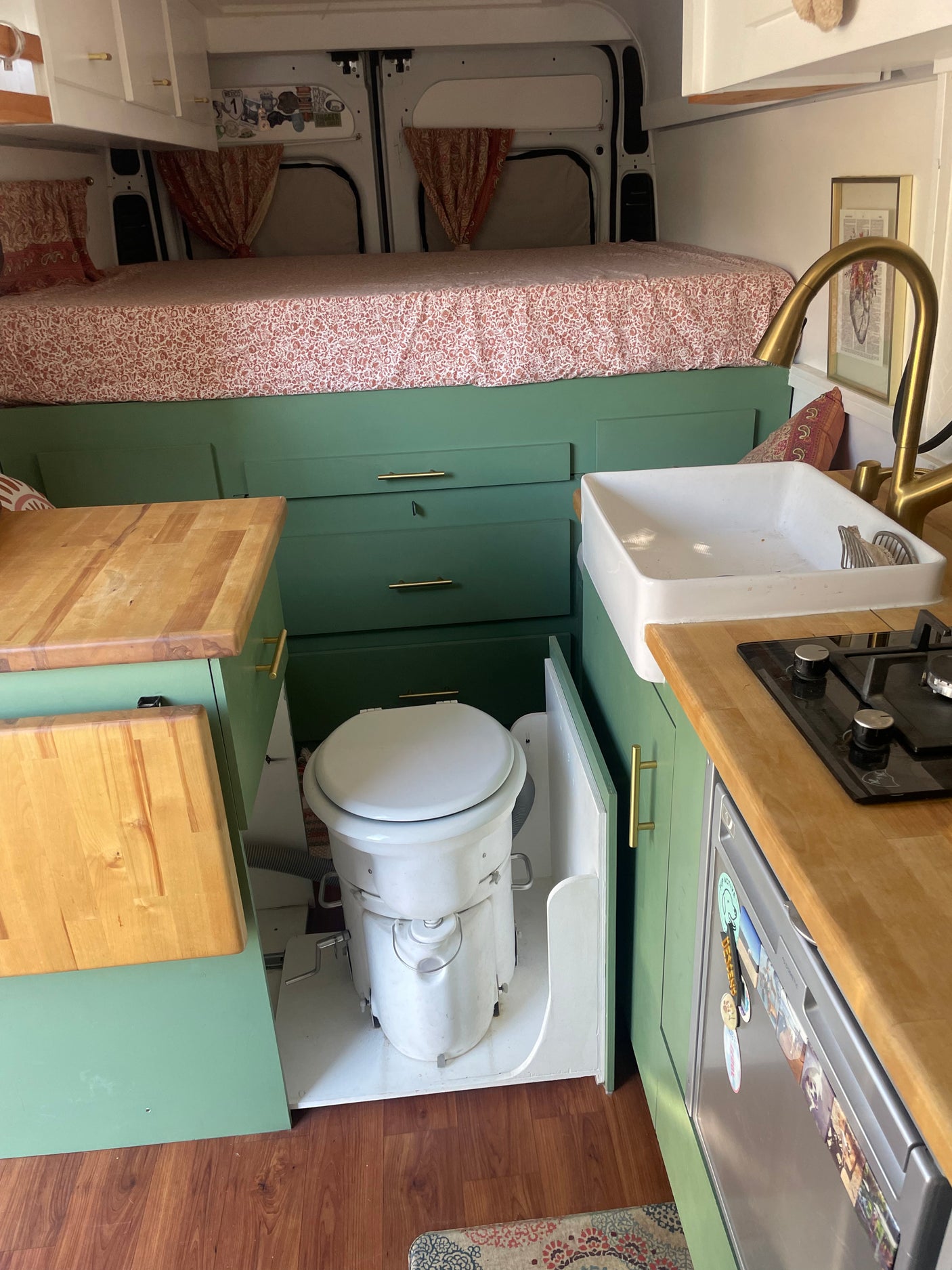 Inside this RV rental: a stylish van conversion with a raised bed, green kitchen cabinets, sink, stove, and pull-out toilet.