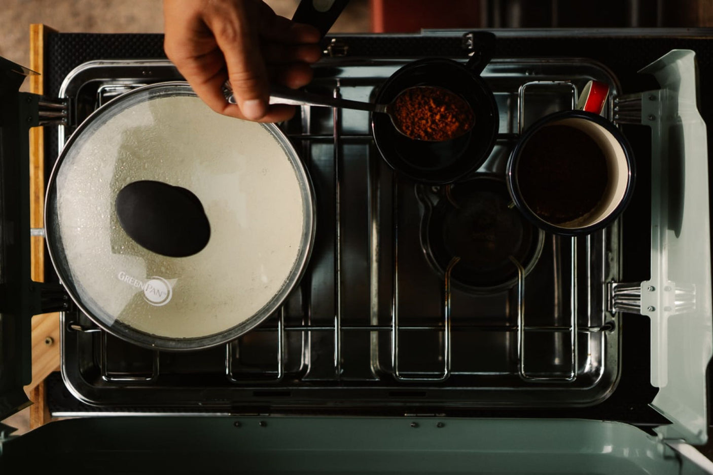 Morning cooking in an RV rental: overhead view of a compact stove with a covered pan, coffee, and spices.