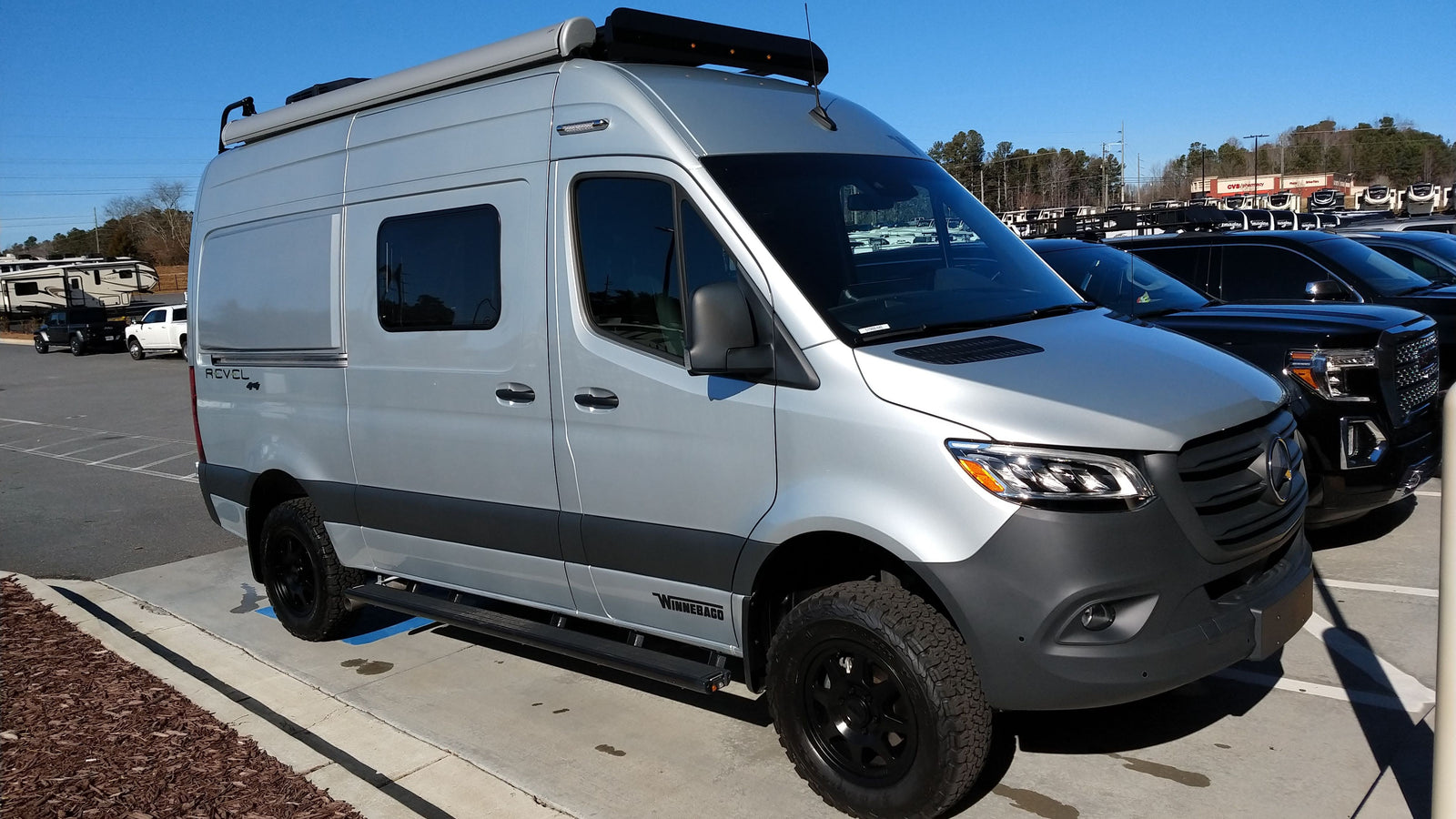 Silver Winnebago Revel camper van, ideal for RV rental adventures, parked outdoors on a sunny day.