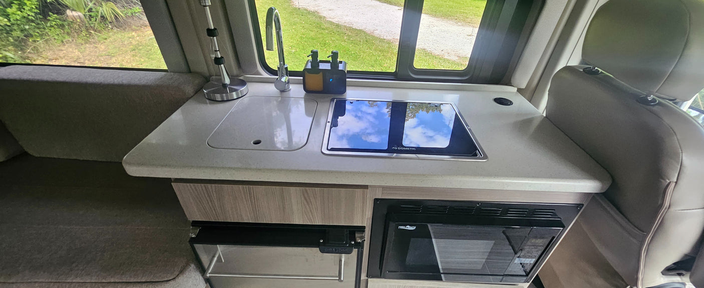 Inside an **rv rental**, a compact kitchenette features a sink, Dometic stovetop, microwave, and fridge, ideal for travel.