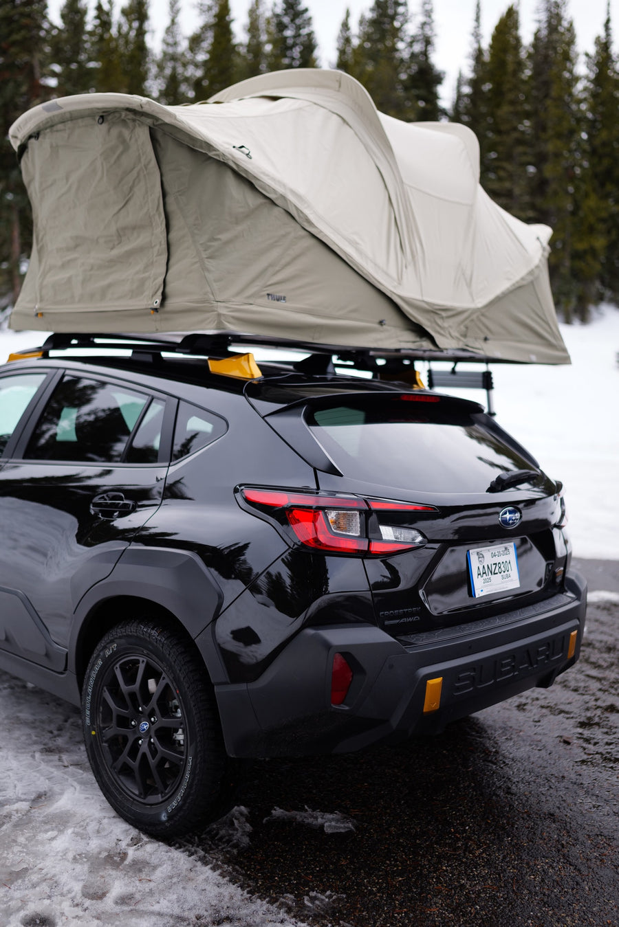 Black Subaru Crosstrek with a Thule rooftop tent, parked in a snowy forest, an agile option for an RV rental adventure.