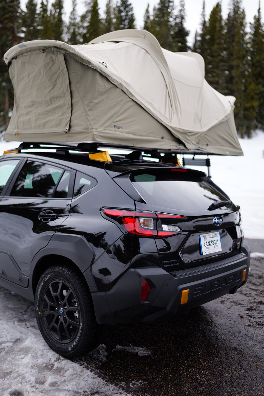Black Subaru Crosstrek with a Thule rooftop tent, parked in a snowy forest, an agile option for an RV rental adventure.