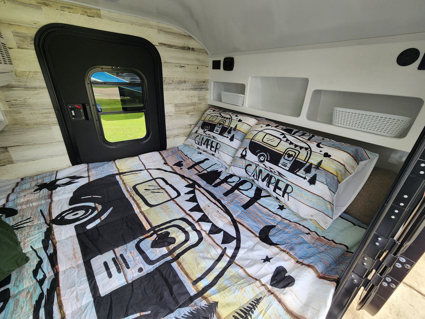Cozy RV rental interior with a "Happy Camper" bed, storage cubbies, and a side door.