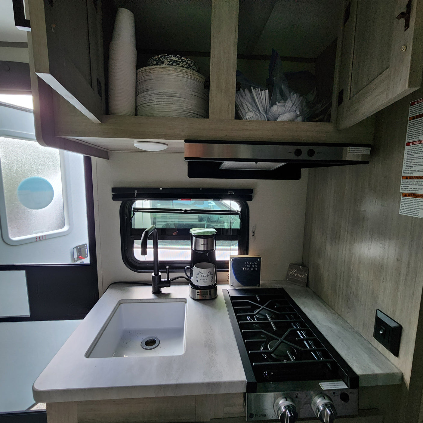 Inside an RV rental, showing the compact kitchen (galley) with sink, stove, coffee maker, and storage cabinets.