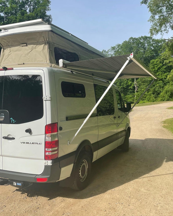 on a dirt road. Ready for your next RV rental adventure!|White Mercedes Sprinter RV rental with a pop-top and extended awning on a dirt road