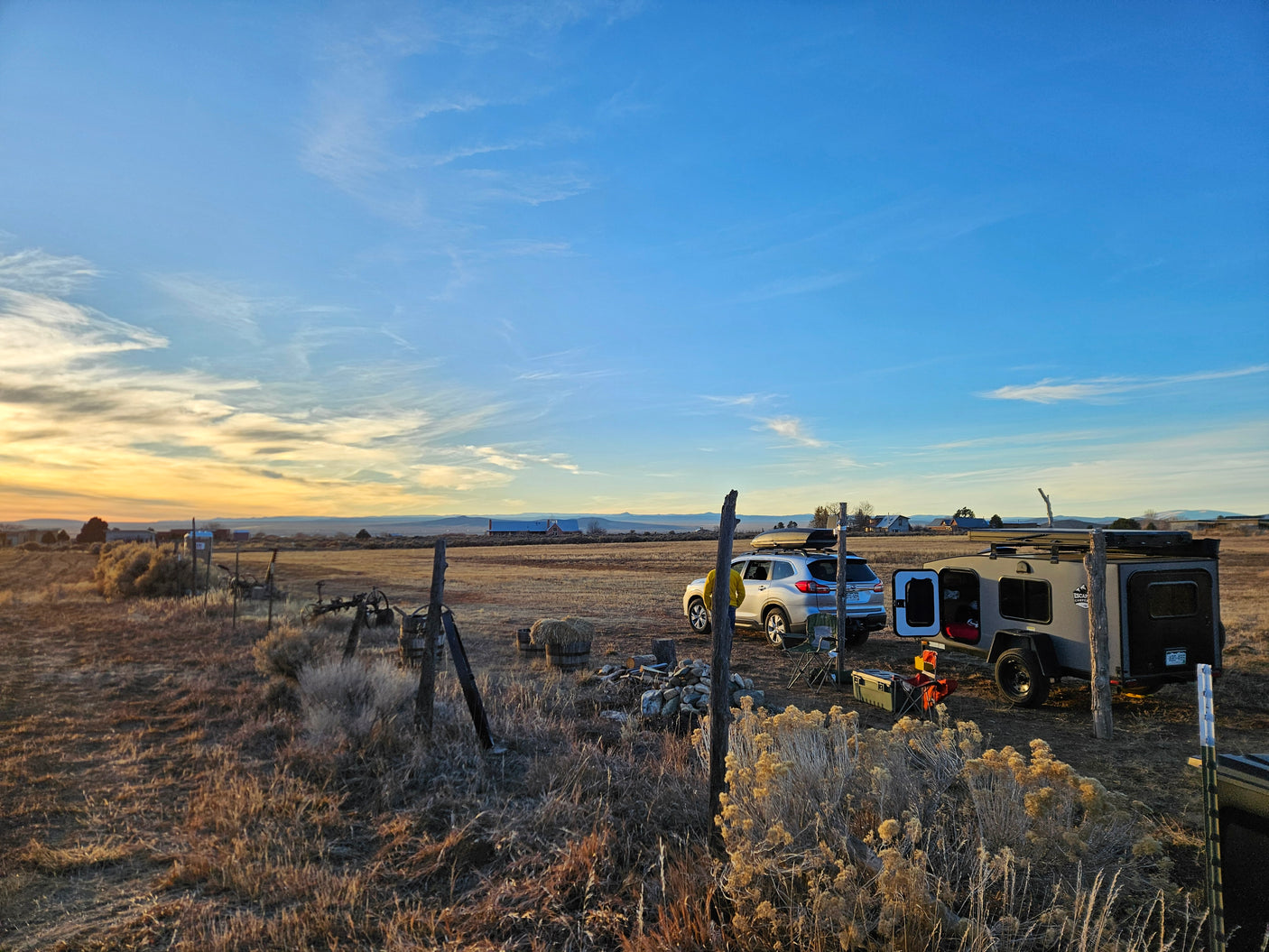 Rural sunset camping: a Subaru and Escape Camper RV rental trailer in a dry field, ready for an outdoor adventure.