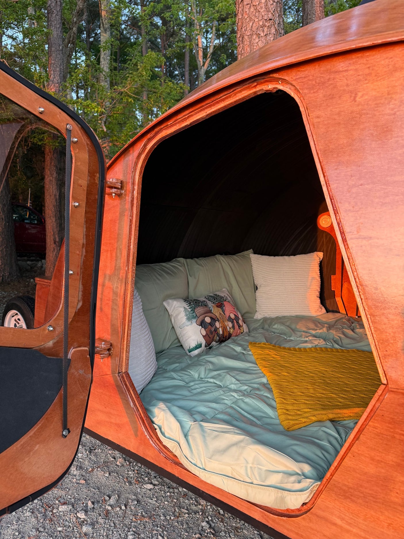 and a shore beyond.|An rv rental's open kitchen provides a cozy cooking spot with stunning lake sunset views. Ideal for lakeside camping.|Cozy teardrop RV rental interior with a comfy bed: green linens
