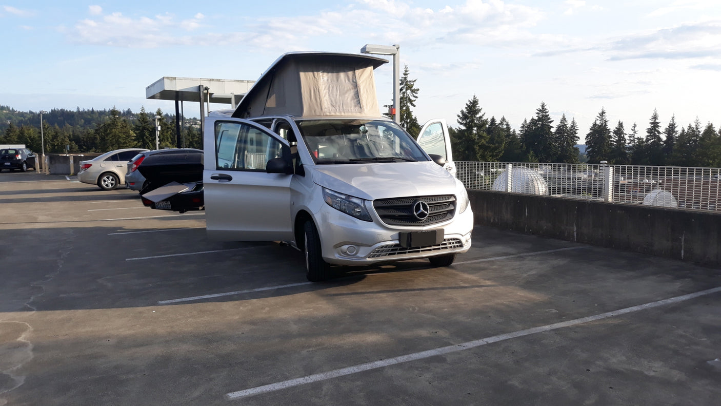 A silver Mercedes-Benz pop-top camper van, ready for adventure as an RV rental, parked on a sunlit concrete lot.