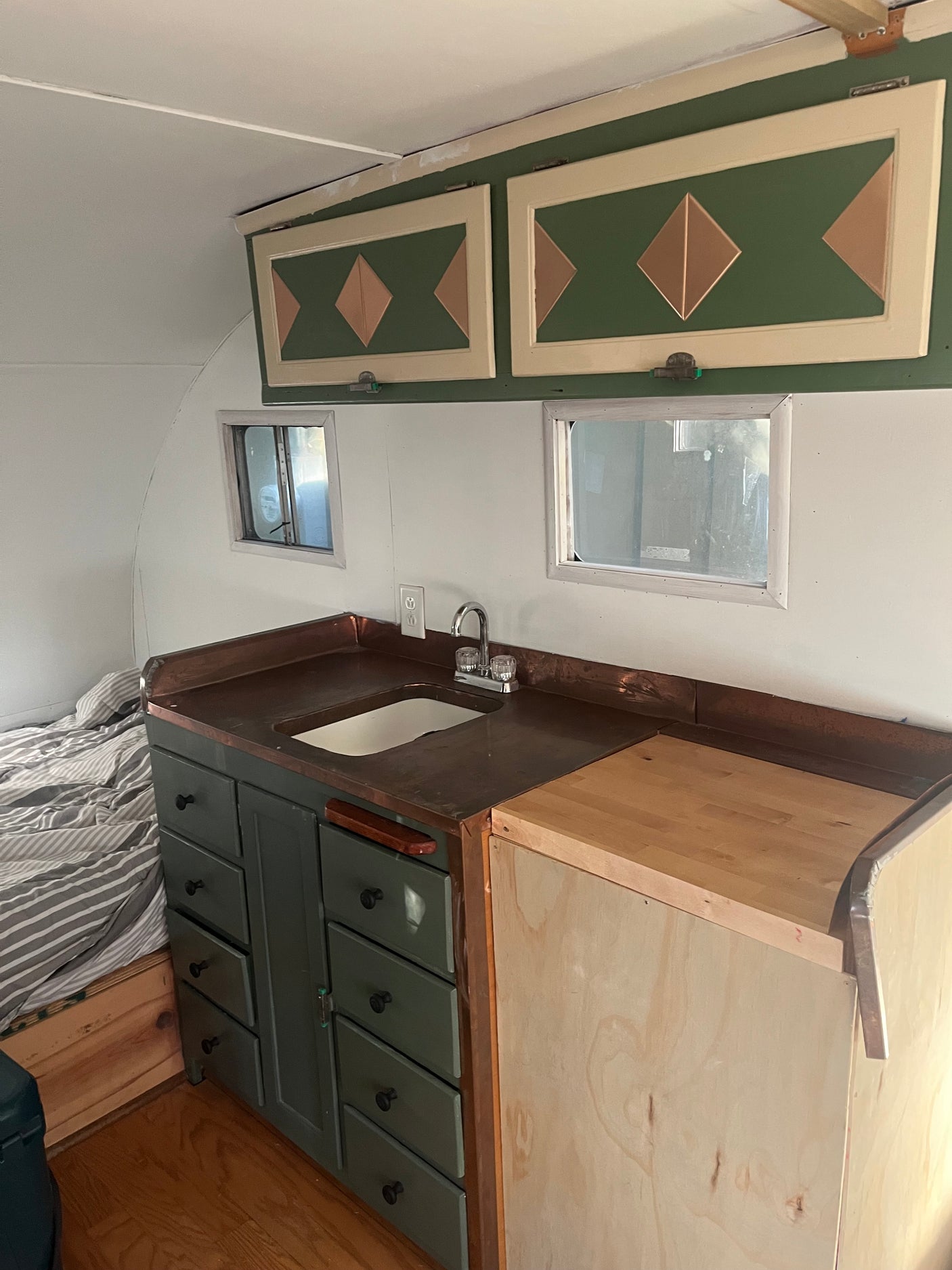 Cozy RV rental interior: custom green kitchen with copper counters, built-in sink, decorative cabinets, and bed.