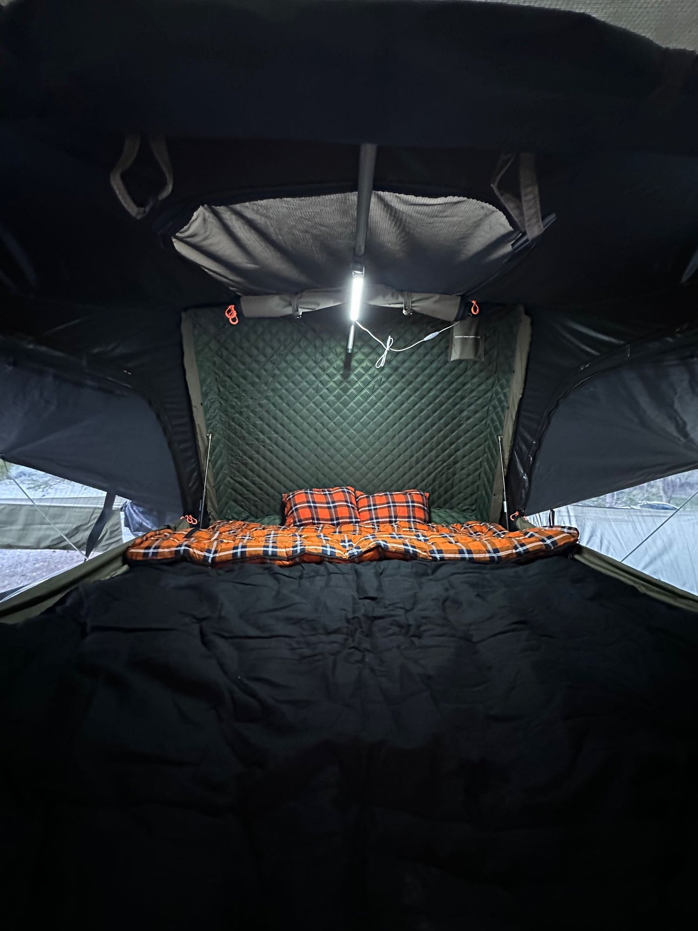 Inside a comfy rooftop tent bed with plaid bedding & bright light. Ideal for rv rental camping.