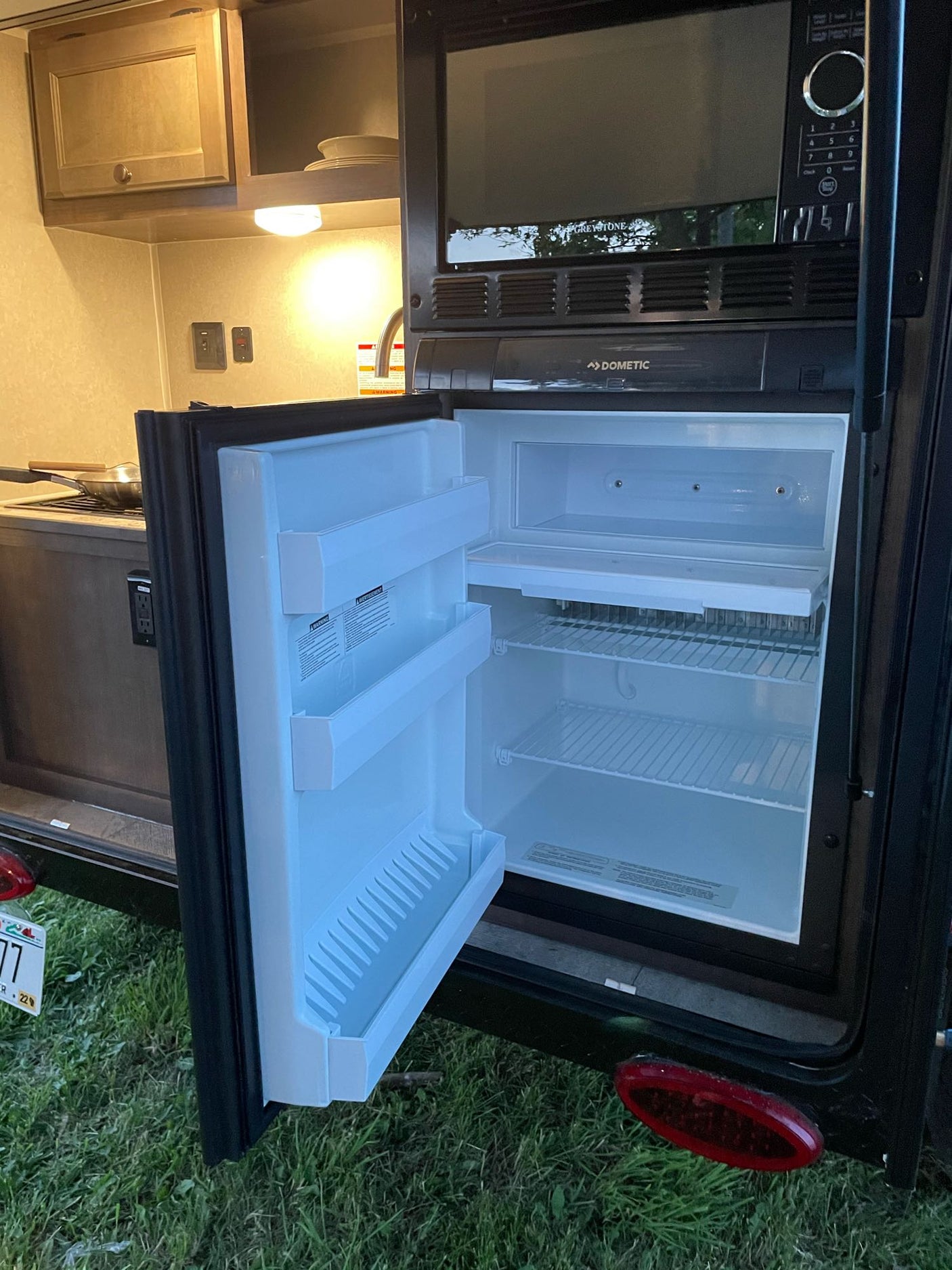 Inside an RV rental, a clean, open refrigerator is ready alongside the microwave and cooking area.