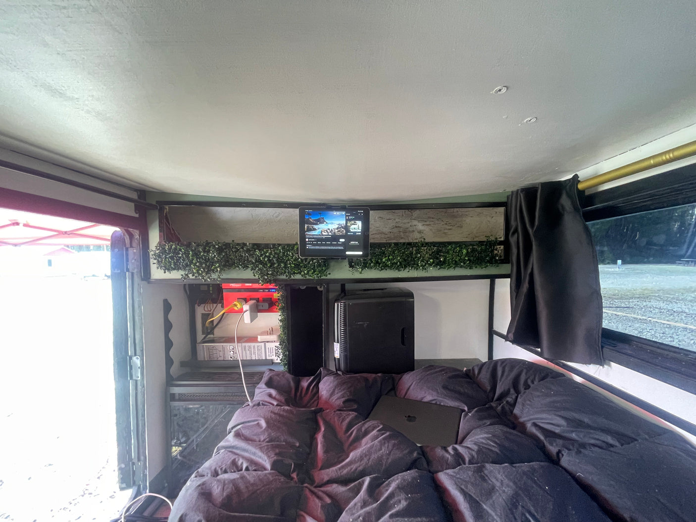 Cozy rv rental interior: bed with laptop, tablet, power strip, and mini-fridge, creating a functional mobile setup.
