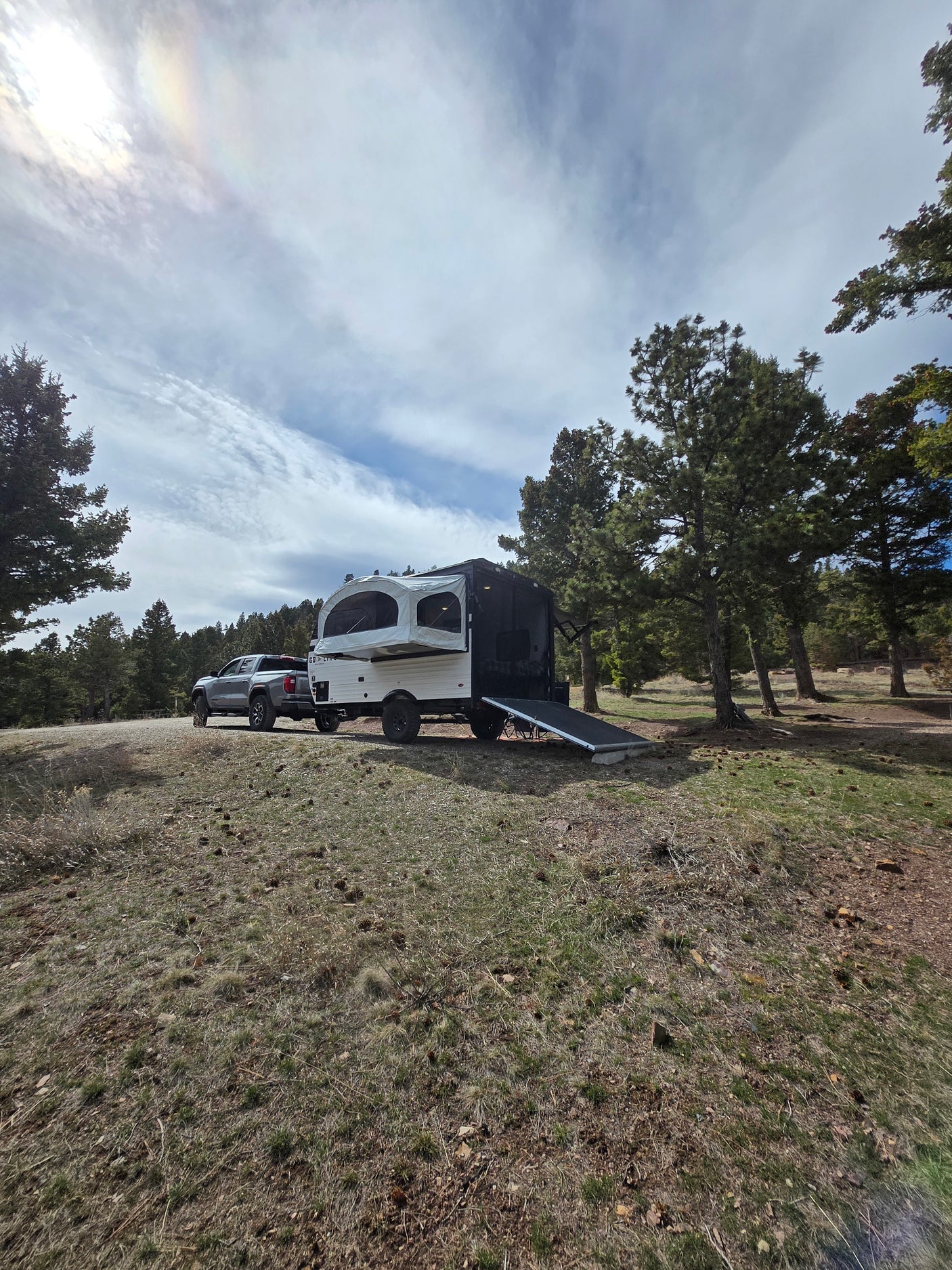 RV rental pop-up trailer & truck ready for adventure at a forest campsite with pine trees under a bright sky.
