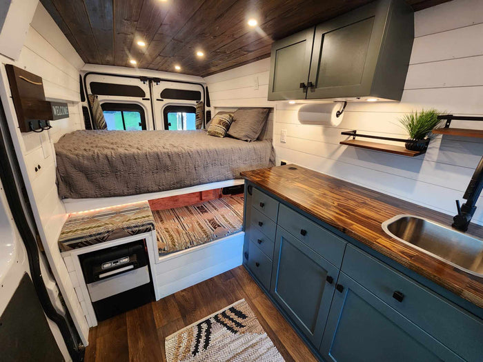 with sandy dunes and ocean visible in the background.|Detailed RV rental interior: raised bed