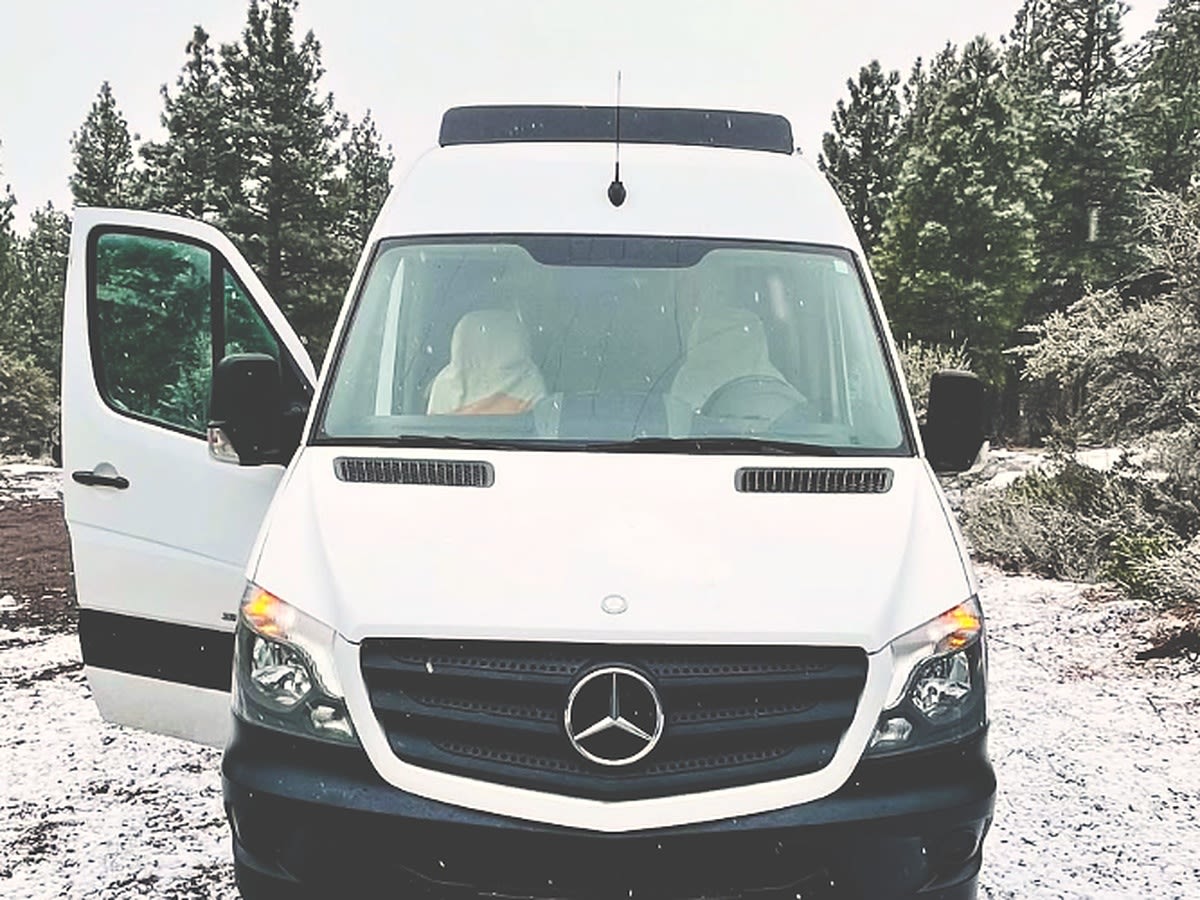 and a comfy bed.|White adventure van with ladder & roof rack in a snowy forest. Perfect for an RV rental road trip.|This RV rental camper van features a well-equipped interior: a raised bed — photo 4