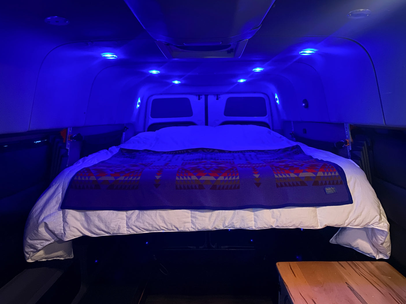 Van conversion RV rental bedroom with a comfortable bed, accented by vibrant blue LED lighting.