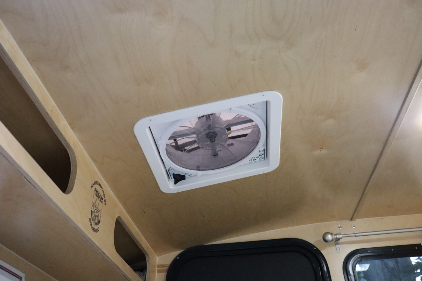 RV rental interior: Light wood ceiling with a central vent fan, overhead storage, and windows.