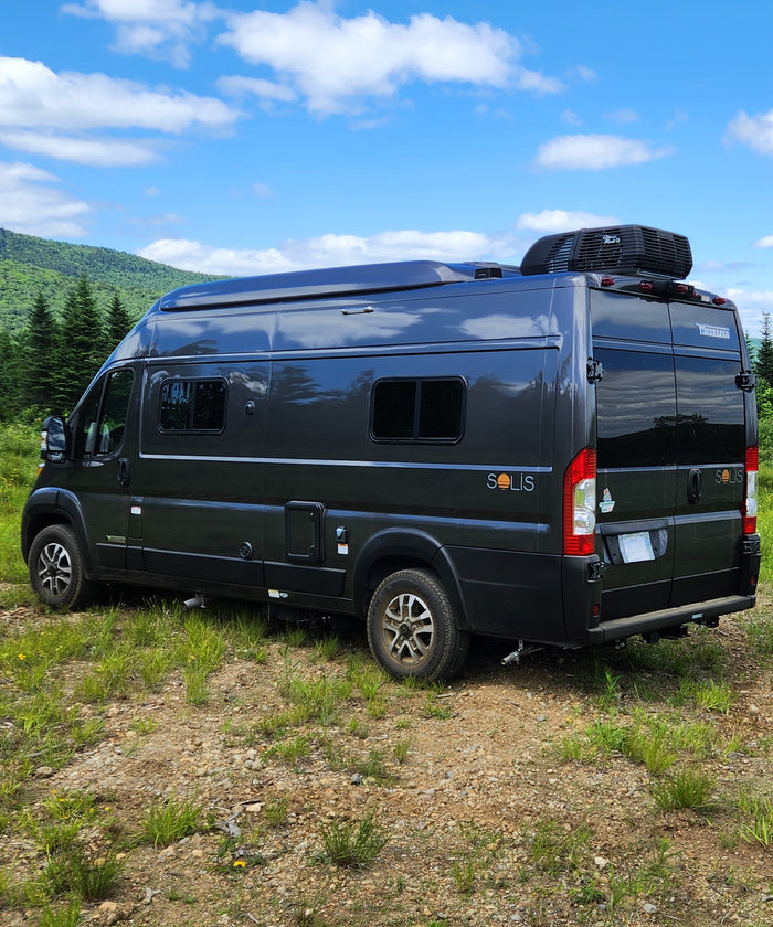 ideal for your next rv rental. Interior visible through windshield; parked by trees.|This dark grey Winnebago Solis camper van is ready for your next rv rental adventure in the mountains.|Rear view of a dark Winnebago Solis **rv rental** parked on a grassy path with green mountains and a blue sky.|Grey pop-top camper van rv rental at a serene campsite. Features a picnic table
