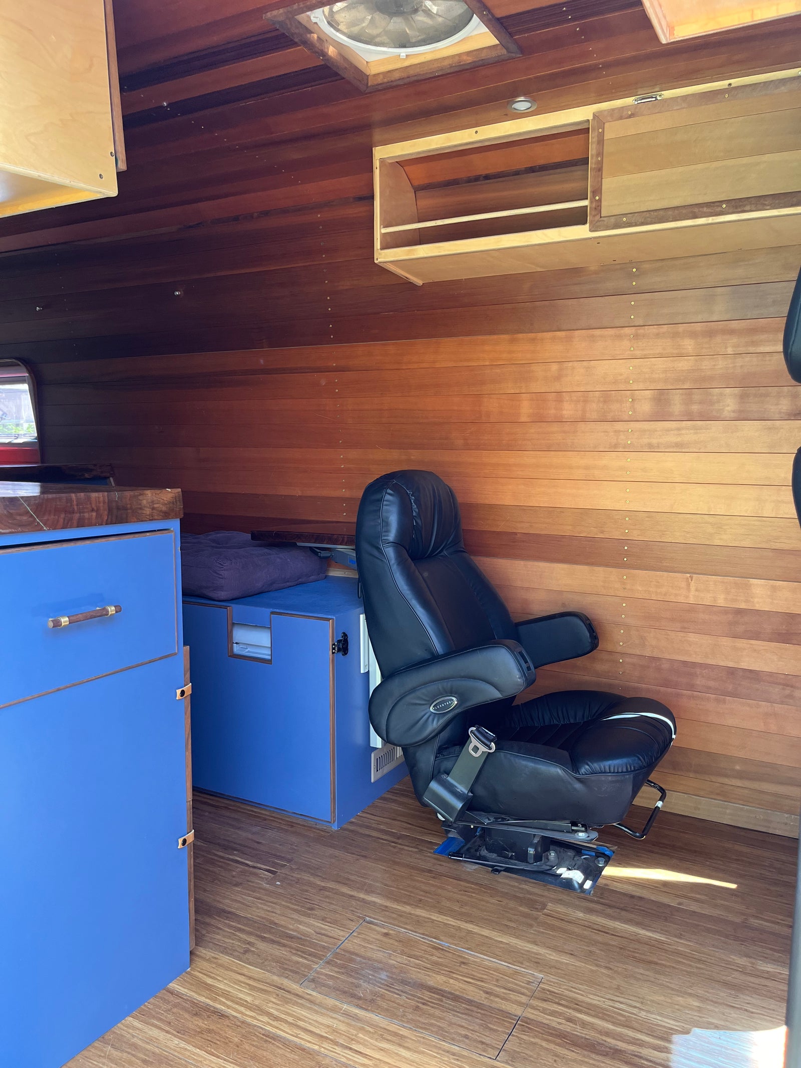 RV rental interior: rich wood walls & ceiling, black leather seating, blue custom cabinets, and a ceiling fan. Cozy comfort.
