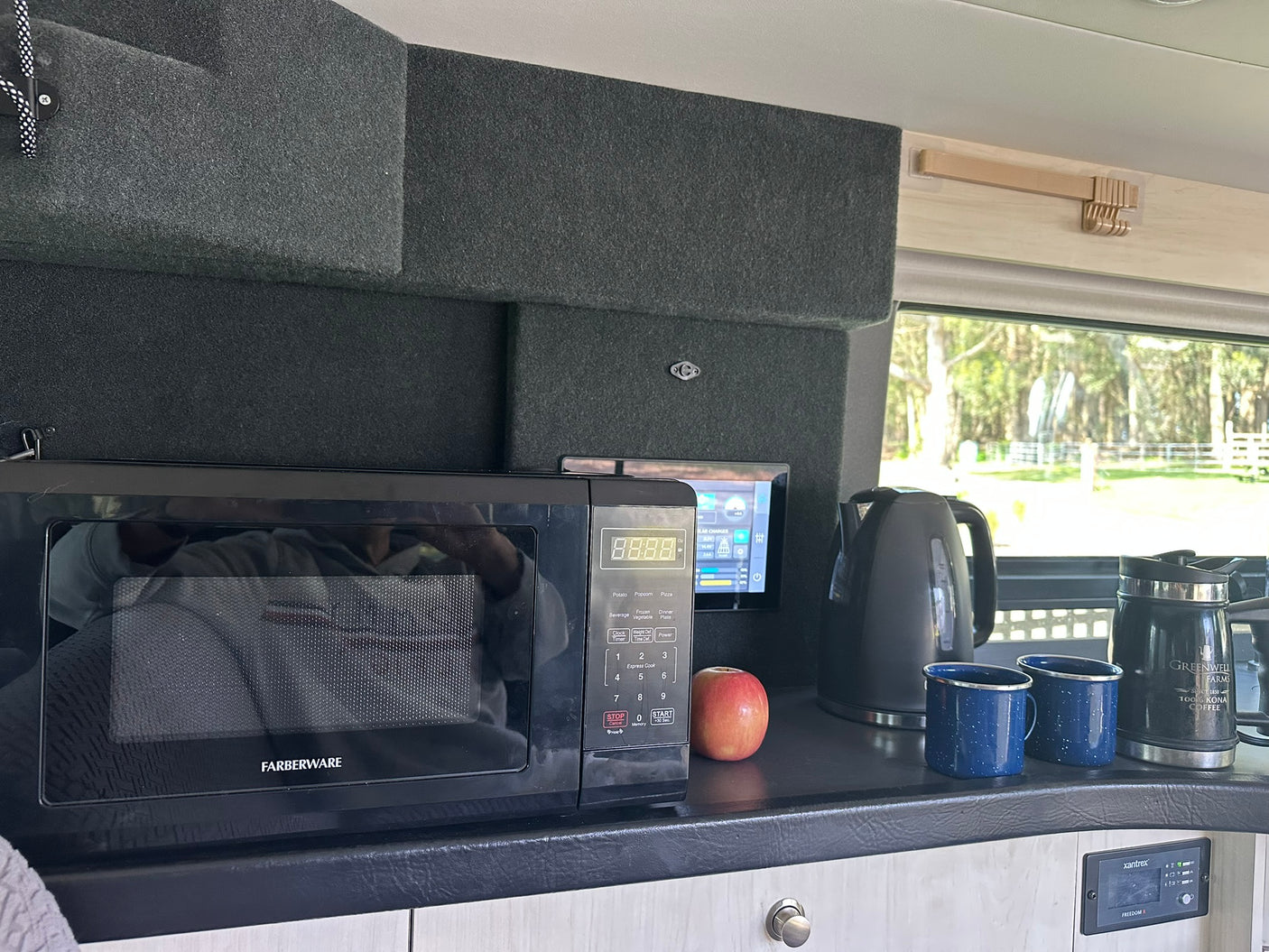 RV rental kitchen counter featuring a microwave, kettle, two blue mugs, and Kona coffee container.