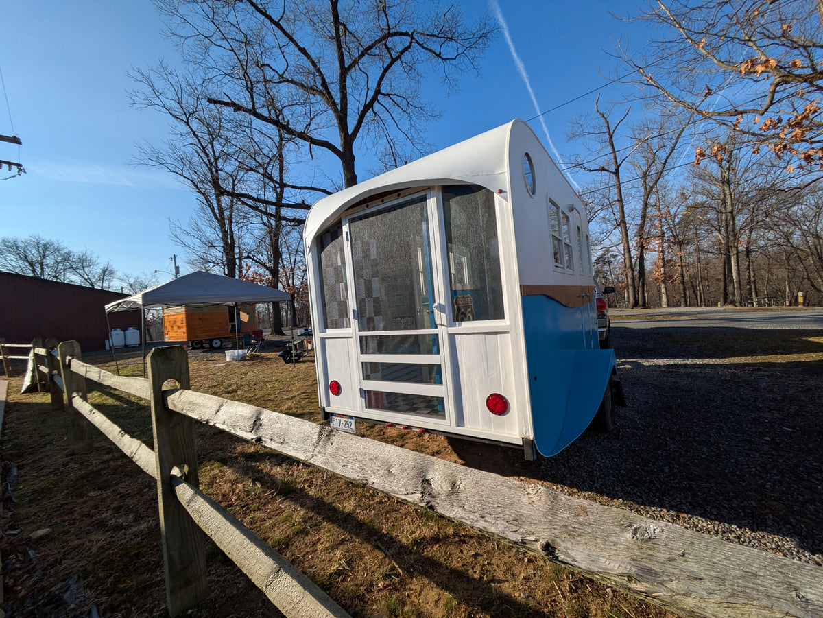 Unique blue & white custom RV rental, resembling a tiny home, parked by a wooden fence under a clear sky. — photo 9
