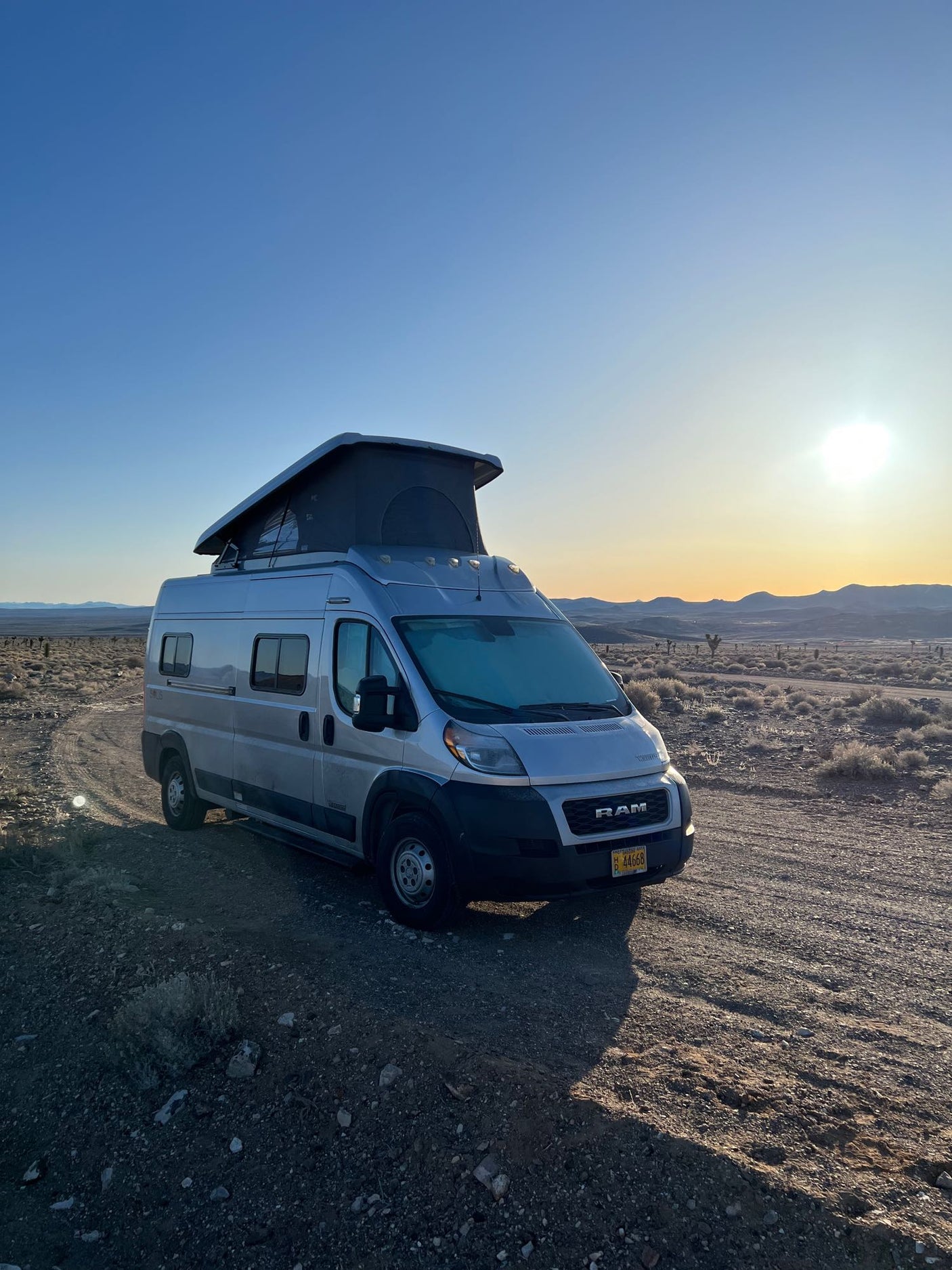 Golden hour desert escape in an RV rental. A silver pop-top camper van sits on a dirt track, ready for van life travel.