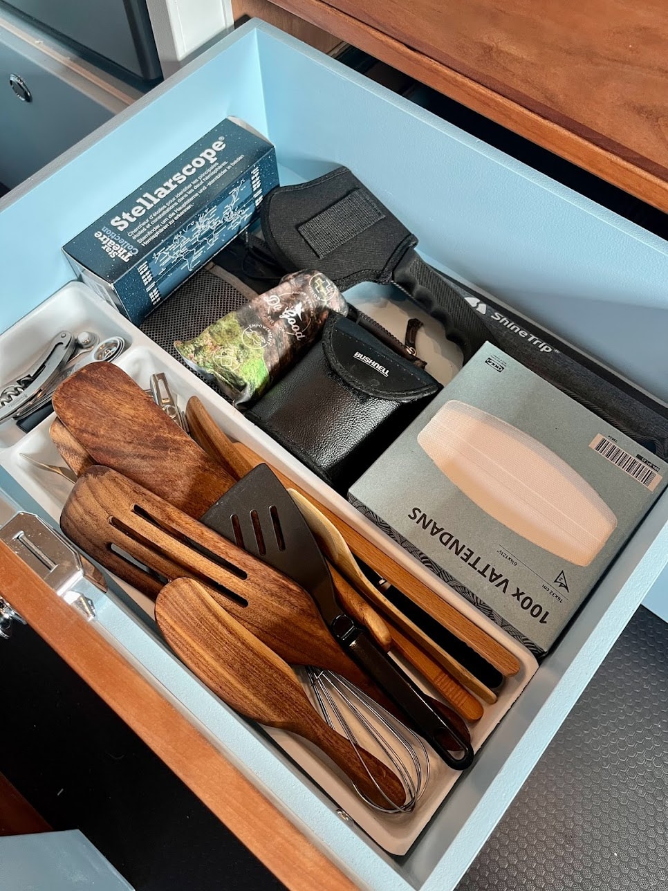 Neatly organized RV rental drawer with kitchen utensils, a Stellarscope, Bushnell gear, and travel supplies.