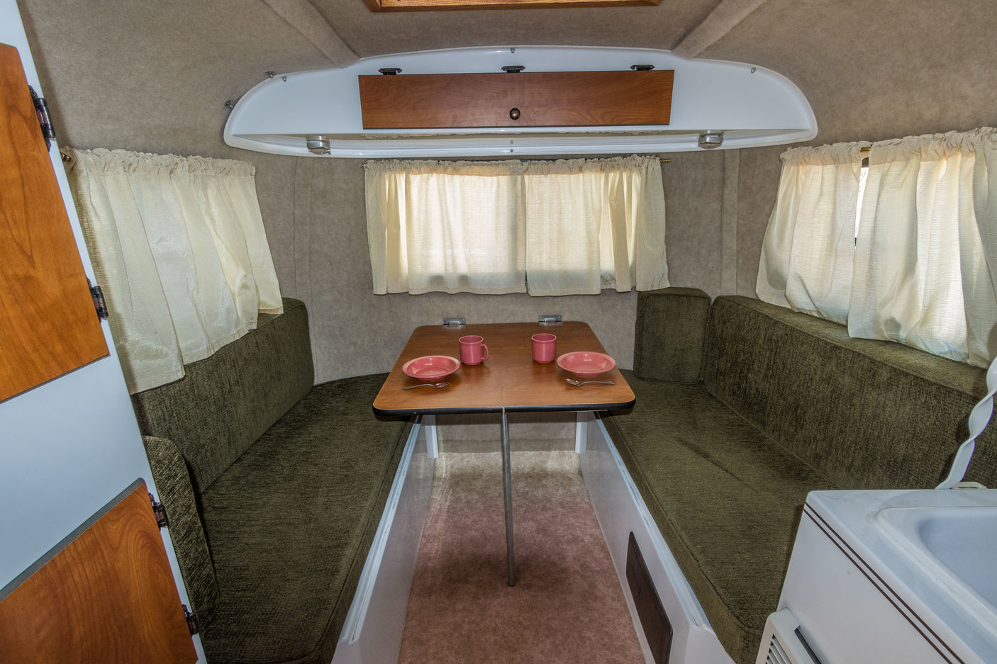 Inviting RV rental interior featuring a cozy dining nook with olive green benches & wood table set with pink dishes.