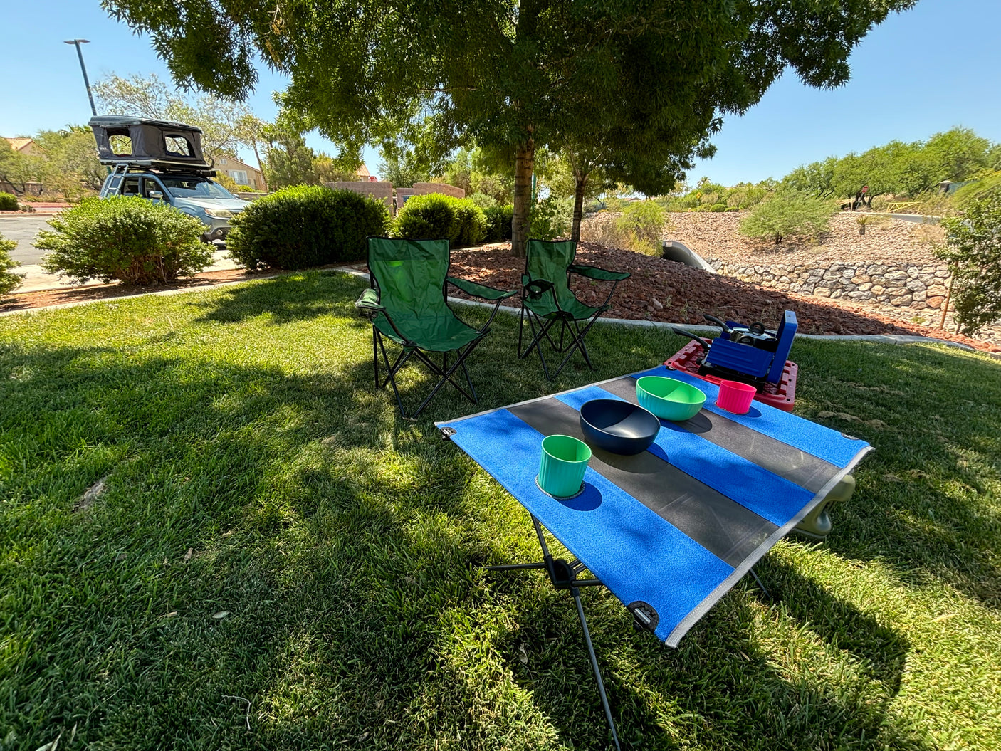 Camping setup with SUV, roof-top tent, chairs, and table on grass. Great for an RV rental trip.