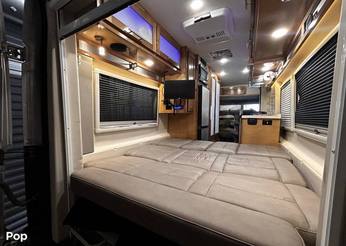 Inside an **rv rental**: a cozy bed with window blinds, compact kitchen, and overhead storage. Perfect for travel adventures.
