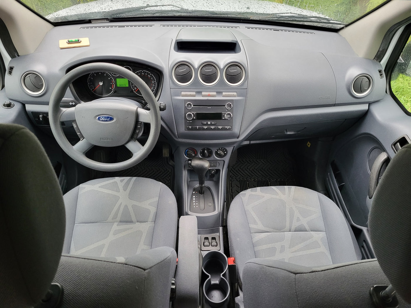 parked on gravel surrounded by tall trees at a sunny campsite.|Ford Transit Connect van interior: dashboard — photo 2