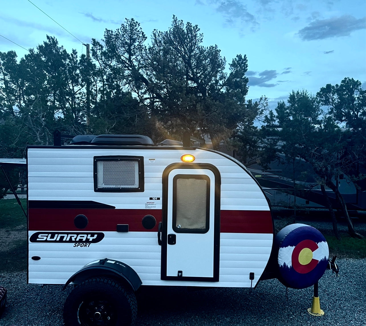 This compact Sunray Sport travel trailer, white with red stripes, is parked at a campsite. Ideal for your next RV rental adventure.