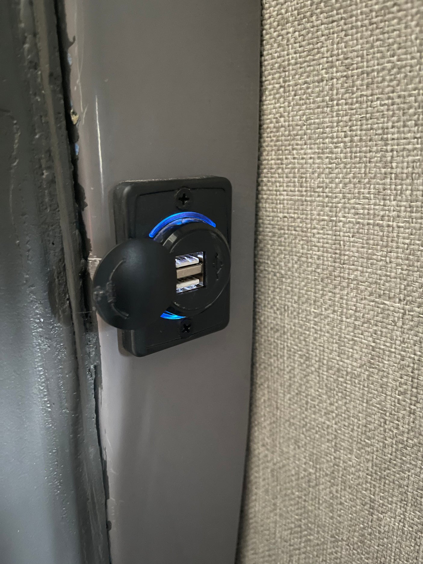 This RV rental features a dual USB charging port with a blue LED, mounted on a gray panel next to a textured wall.