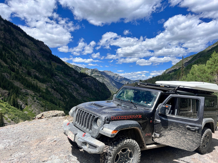 Mud-splattered Jeep Mojave with rooftop tent on a mountain trail, ideal for an RV rental adventure.