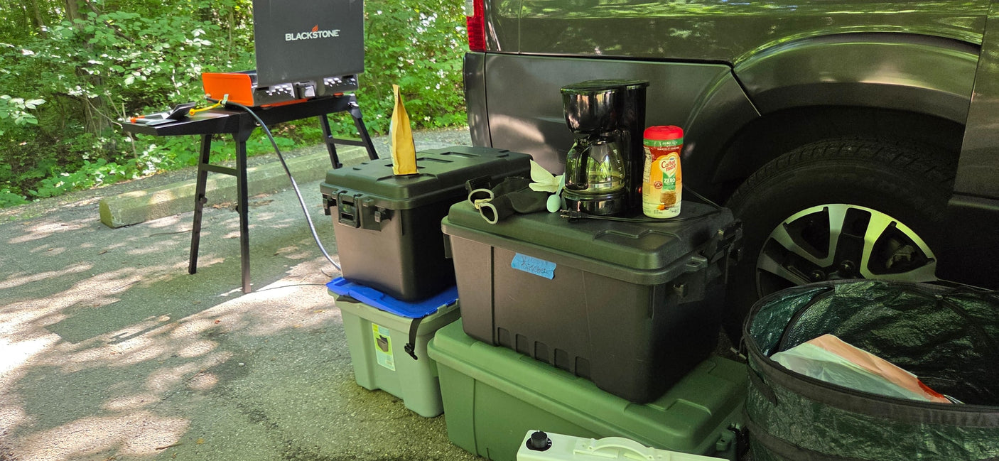 Outdoor kitchen setup featuring a Blackstone griddle, coffee maker, and storage bins next to an RV rental vehicle for camping convenience.