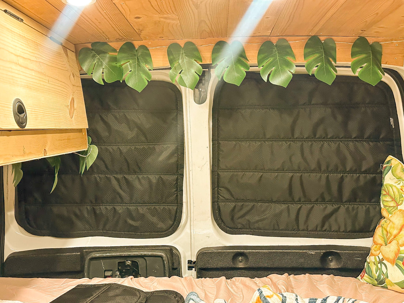 Inside this **rv rental** camper van: wooden ceiling, insulated window blinds, tropical leaf decor, and a comfy bed.